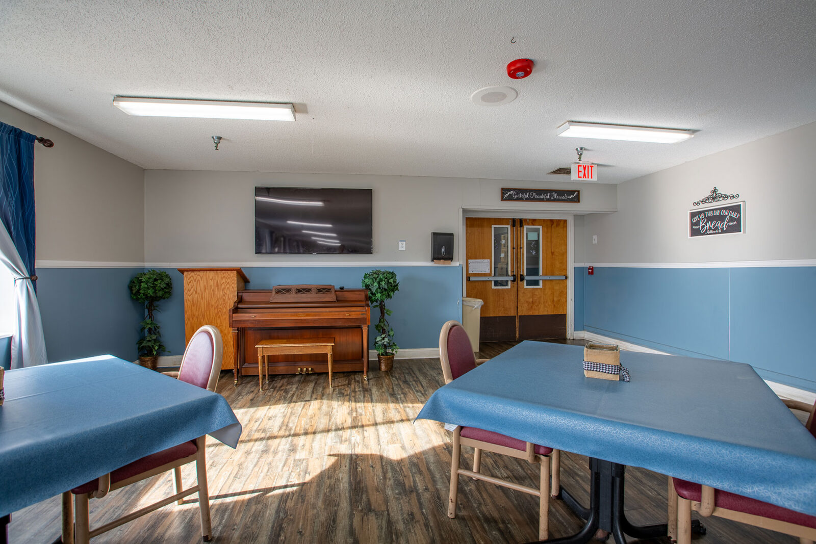 Bright room with piano, tables, and television on wall.